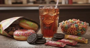 Un vaso de bebida azucarada junto a alimentos ultraprocesados altos en azúcar añadida.