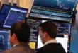 Operadores financieros analizando gráficos de cotizaciones de Wall Street en pantallas gigantes durante una sesión de alta volatilidad